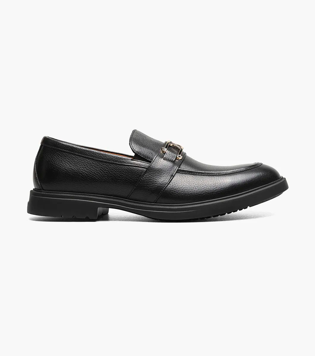 The Stacy Adams Todridge Moc Toe Bit Slip On in black tumbled leather features a gold metal accent, cushioned footbed, tan lining, and black rubber sole.