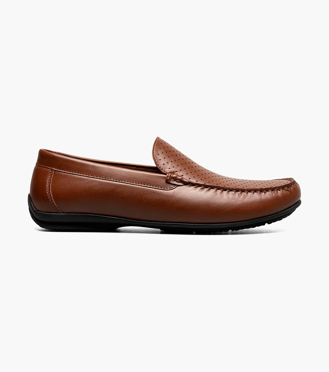 The STACY ADAMS Conroy Moc Toe Perf Slip On in Cognac (25702-221) is a brown leather loafer with a perforated upper, black sole, moccasin-style stitching, and cushioned footbed, shown side profile on a white background.