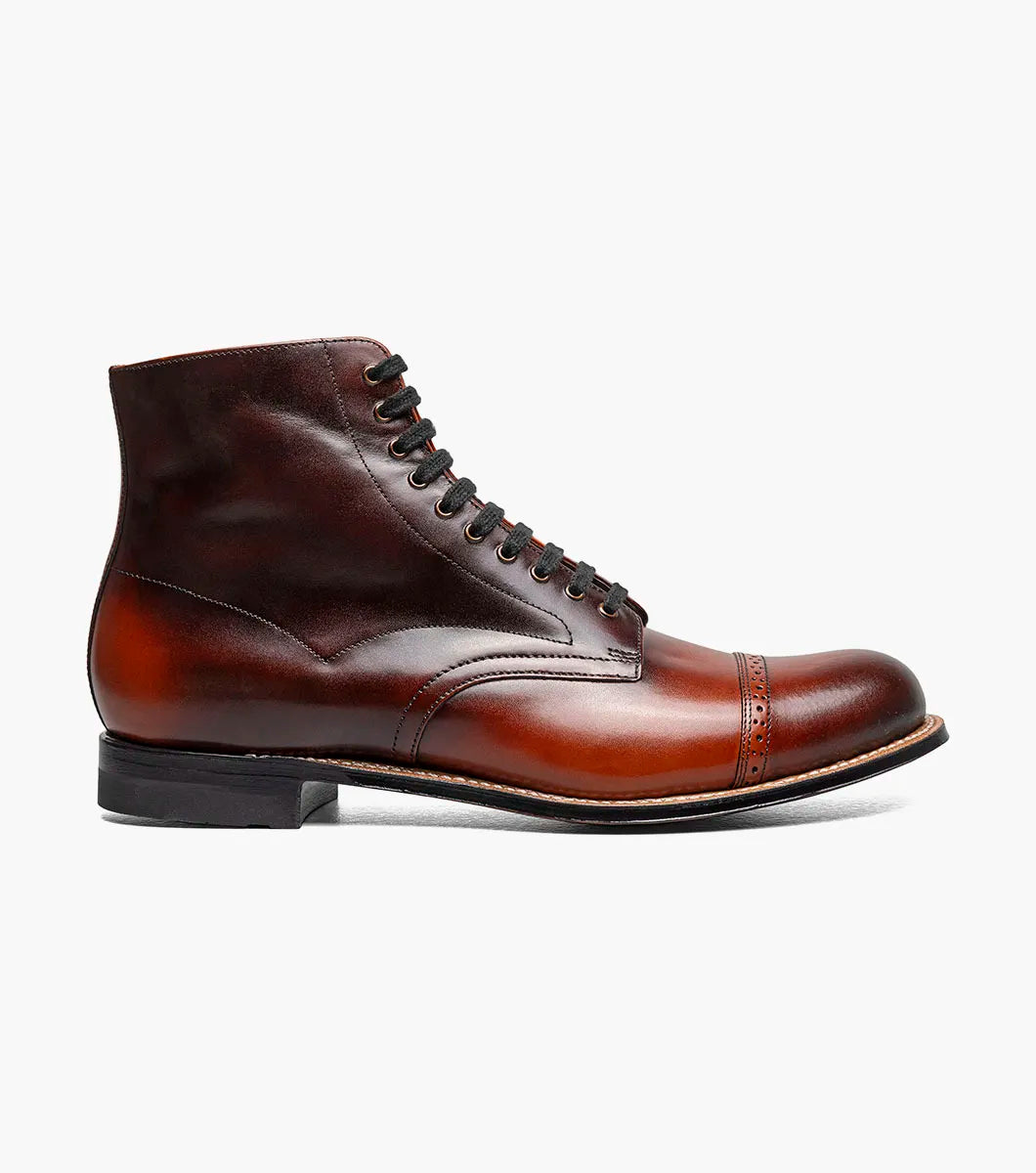 The Stacy Adams Madison Cap Toe Lace Up Boot in Cognac (00110-221) features brown leather, black laces, brogue detailing, and a stacked heel. This stylish STACY ADAMS boot is shown on a white background.