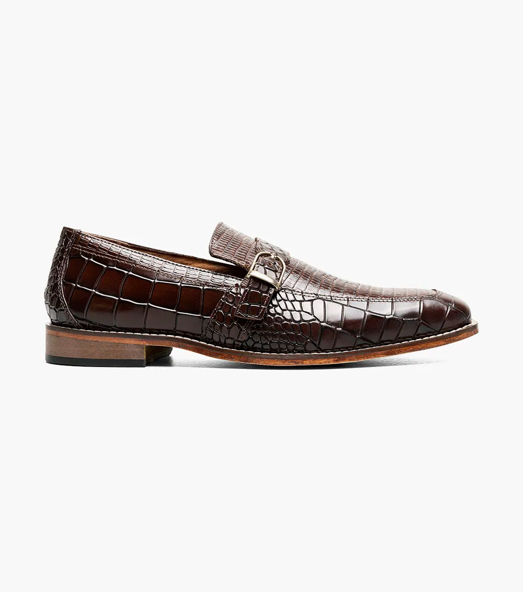 The Stacy Adams Rubiano Moc Toe Buckle Strap Slip On in brown (style 25787-200) by STACY ADAMS is a single leather loafer featuring a crocodile print, slip-on design, side buckle detail, and low heel, displayed on a white background.