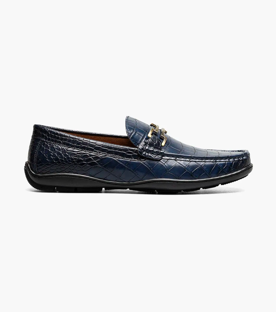 The Stacy Adams Embrey Moc Toe Bit Slip On in navy features crocodile print, a cushioned footbed, black sole, and metal bit detail on the upper, displayed side view on a white background.
