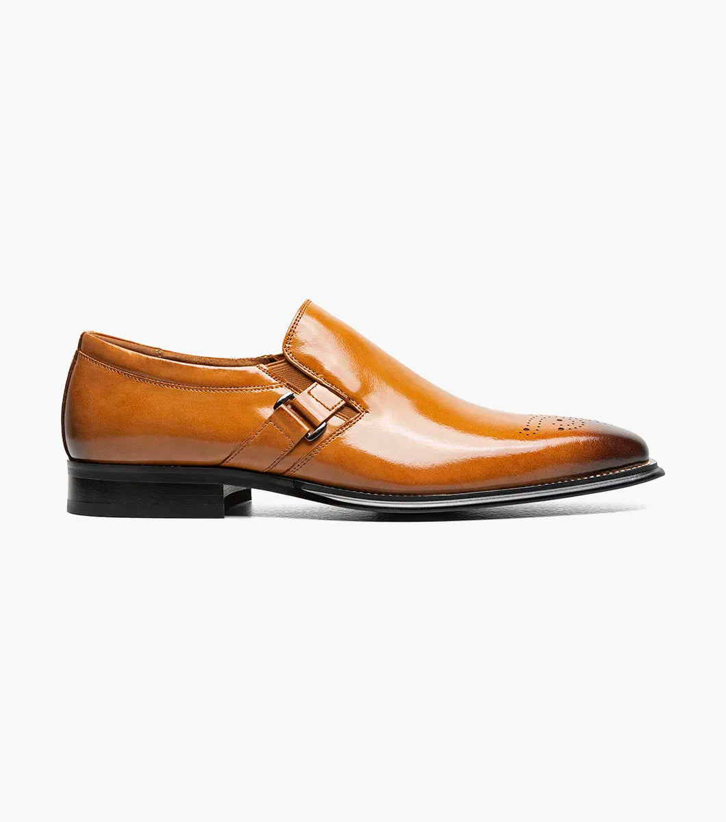 The Stacy Adams Alistair Plain Toe Ornament Slip On (Tan, 25792-240) by STACY ADAMS is a single tan calf leather dress shoe with a pointed toe, decorative perforations, and a side buckle, featuring a comfortable memory foam insole, displayed on a white background.