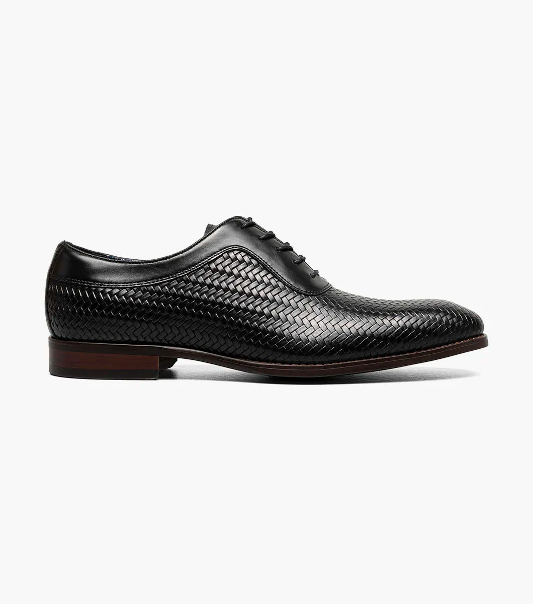 The Stacy Adams Keating Plain Toe Oxford (25709-001) is a black leather dress shoe with a woven pattern, closed lacing, cushioned footbed, and brown sole by STACY ADAMS, shown on a white background.