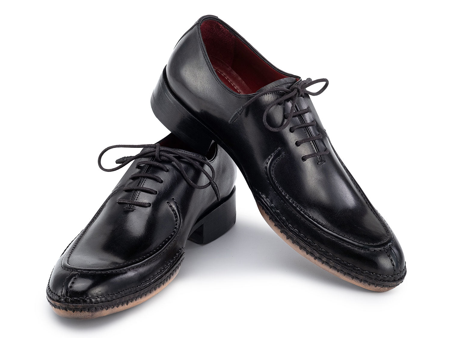 The Paul Parkman Opanka Stitched Men's Split-Toe Black Leather Oxford Shoes (054-BLK) are shown on a white background, one upright and the other leaning, both crafted from hand-painted leather with laces.