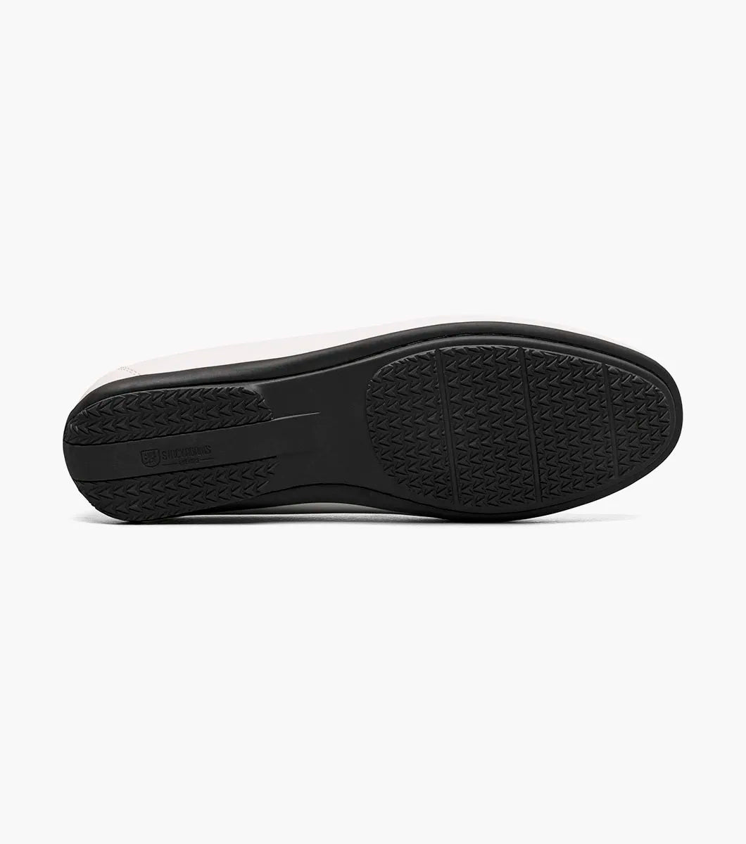 The Stacy Adams Conroy Moc Toe Perf Slip On in white features a perforated leather upper, visible stitching, black rubber sole, and cushioned footbed for comfort. Shown in side profile on a plain background.