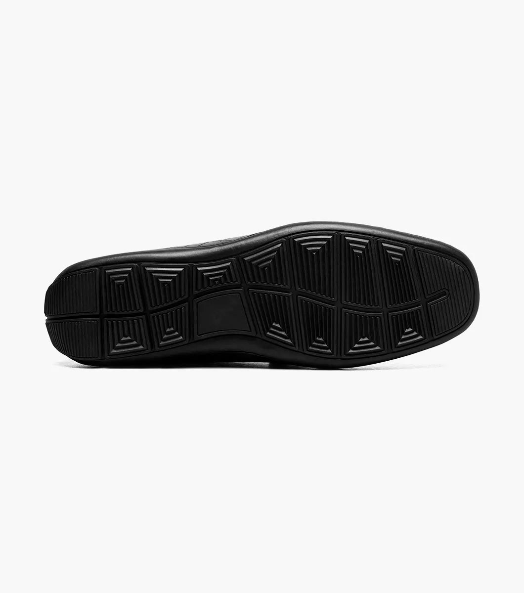 The STACY ADAMS Embrey Moc Toe Bit Slip On (25703-001) is a black leather loafer featuring a crocodile-textured upper and gold metal bit detail, shown in a side profile view.