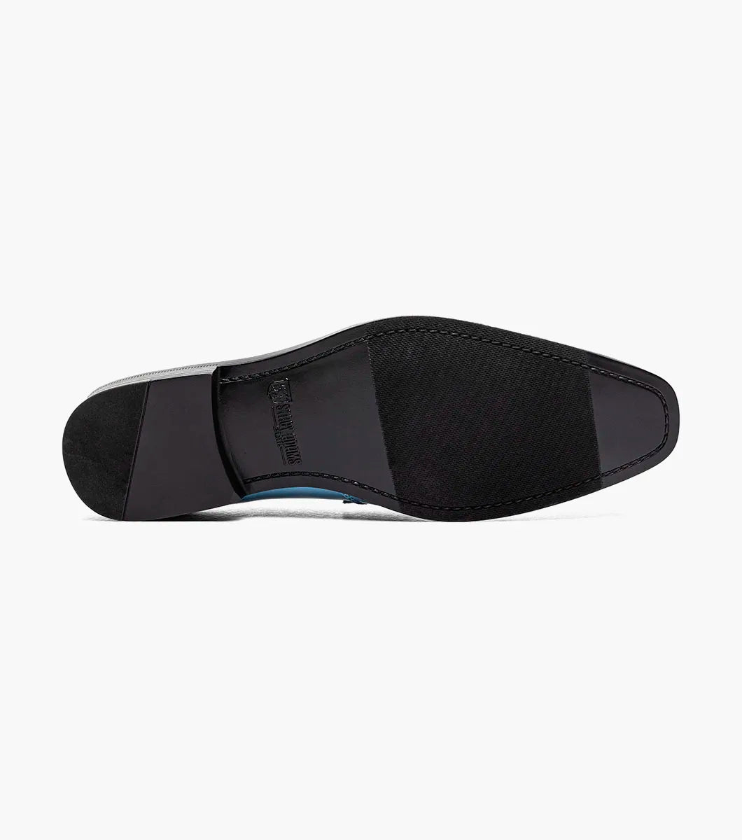 The Stacy Adams Spratley Moc Toe Saddle Slip On in light blue (style 25686-459) showcases a glossy patent leather body with a velour upper, complemented by a matching suede strap and vamp. This men’s loafer by STACY ADAMS features a cushioned insole for enhanced comfort, a black sole, and a low heel, all presented against a plain white background.