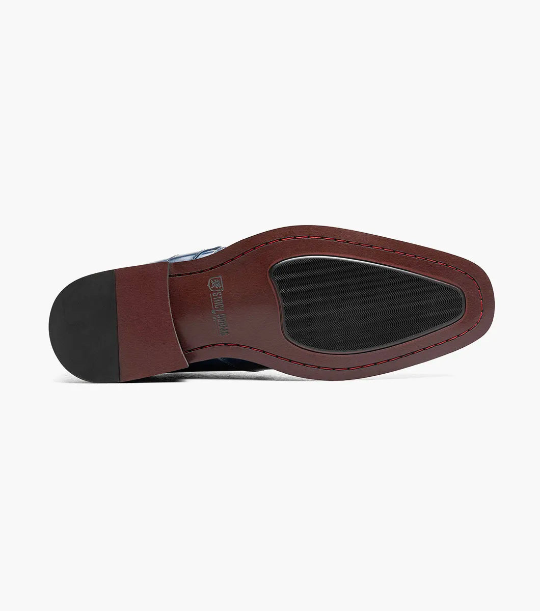 The Stacy Adams Alistair Plain Toe Ornament Slip On in cobalt (style 25792-435) is a single blue calf leather slip-on dress shoe featuring a low heel, decorative perforations on the toe, a side buckle detail, and a comfortable memory foam insole, shown on a white background.