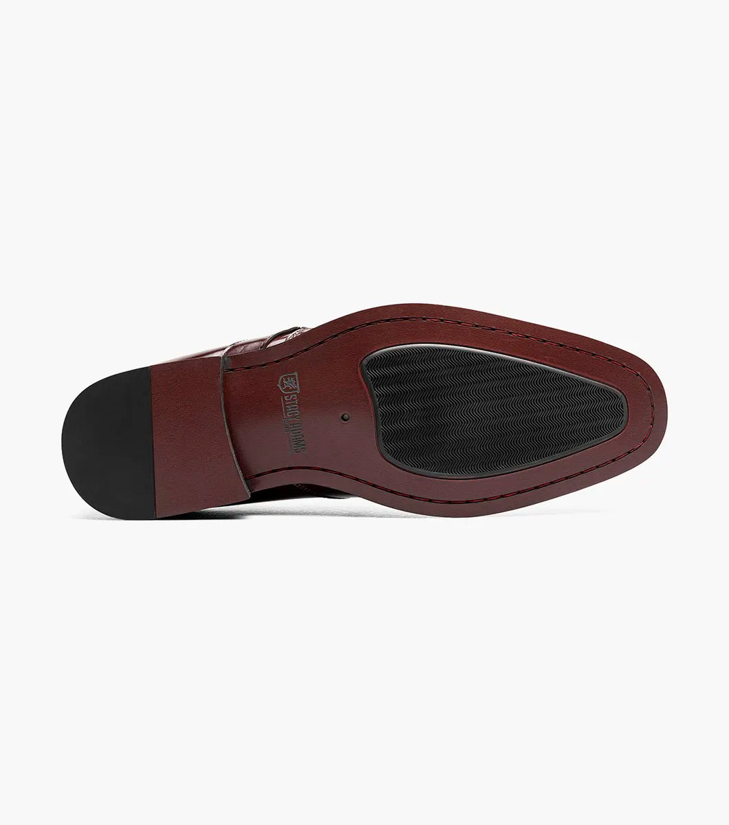 A single STACY ADAMS Alistair Plain Toe Ornament Slip On dress shoe in burgundy, featuring a side buckle detail, perforated toe design, and a comfortable memory foam insole, is displayed on a white background.