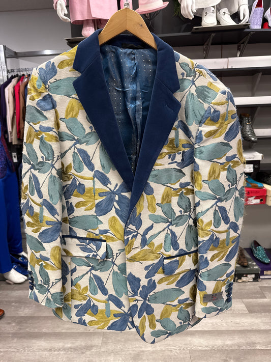 A EJ SAMUEL JACKET 21 CLEARANCE with a blue, green, and yellow leaf print, navy blue velvet lapels, and two front pockets hangs on a wooden hanger in a retail store. Please note: this item is final sale—no returns or exchanges will be accepted.