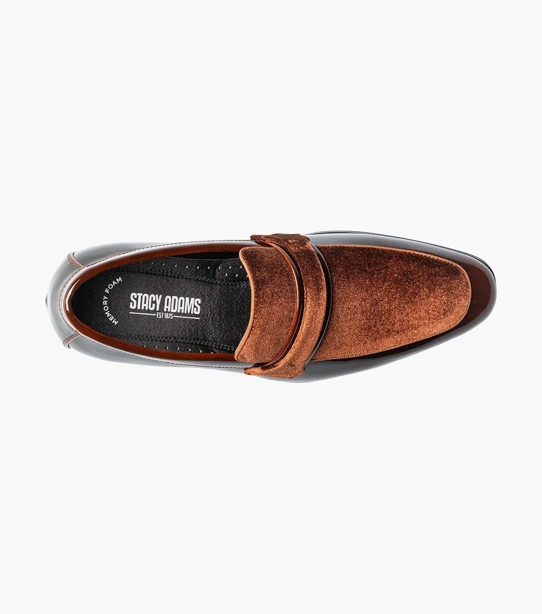 The Stacy Adams Spratley Moc Toe Saddle Slip On (Brown, 25686-200) is a men’s loafer with a glossy leather finish, cushioned insole, and velvet strap detail, displayed angled on a plain white background.