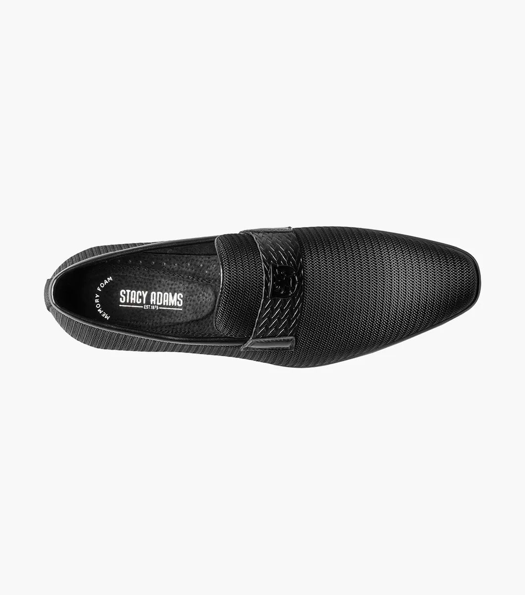 The STACY ADAMS Tazzi Plain Toe Saddle Ornament Slip On (25529-001) is a black textured men’s loafer with leather linings, Memory Foam footbed, decorative saddle band and emblem, and low heel—shown on a plain white background.