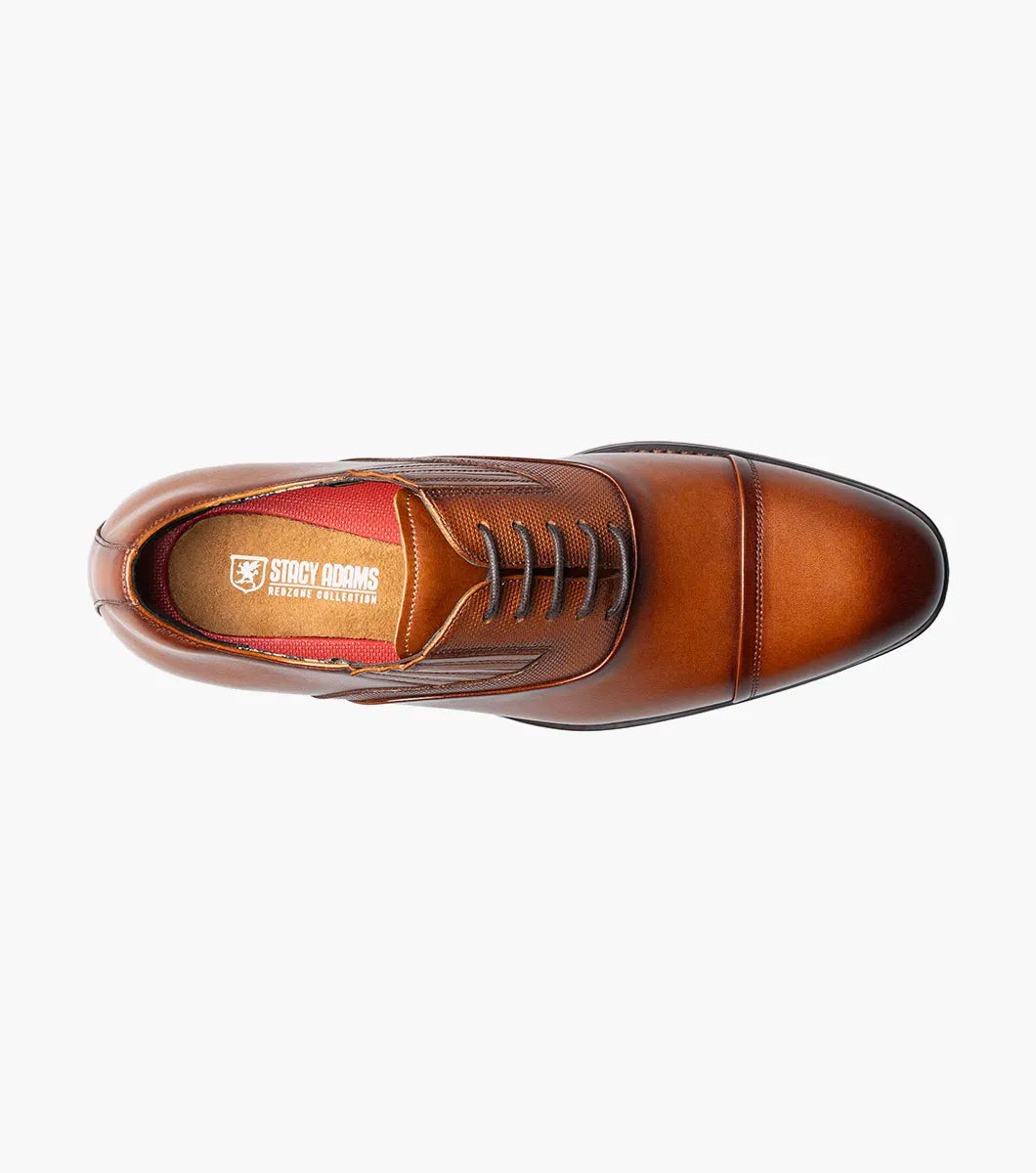 The Stacy Adams Lucas Cap Toe Oxford in Cognac (25766-221) features a brown leather upper with textured side panels, lace-up closure, and low stacked heel for stylish comfort. Men's dress shoe shown on a white background.