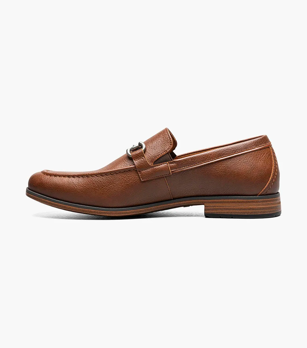 The STACY ADAMS Richmont Moc Toe Bit Slip On in Cognac Tumbled (21567-222) is a brown leather loafer with a metal bit, moc toe slip-on design, low wooden heel, and detailed toe stitching, shown on a white background.