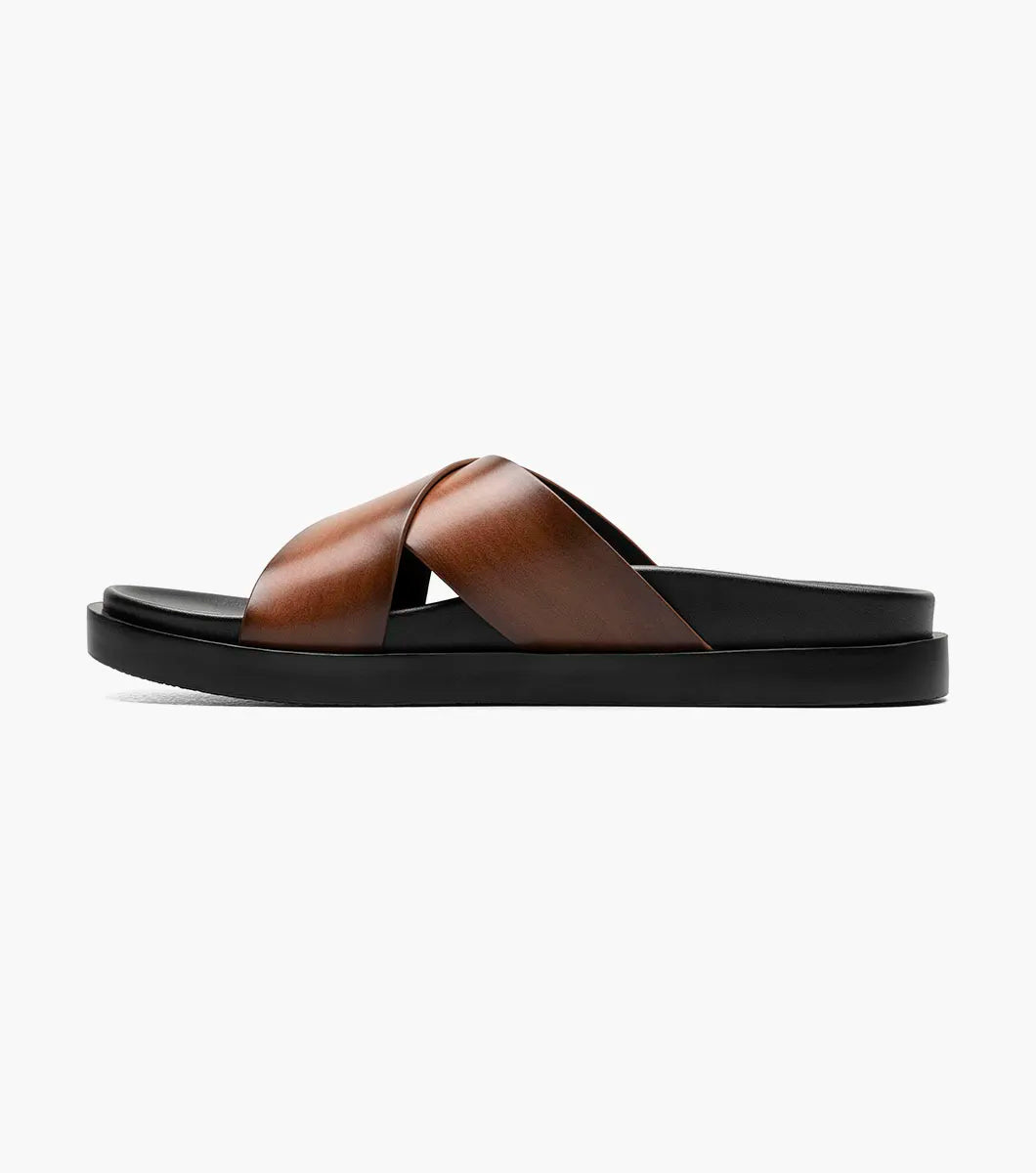 The Stacy Adams Montel Cross Strap Slide Sandal in Cognac (25469-221) features brown leather straps and a black cushioned footbed, perfect for summer. Shown on a white background.