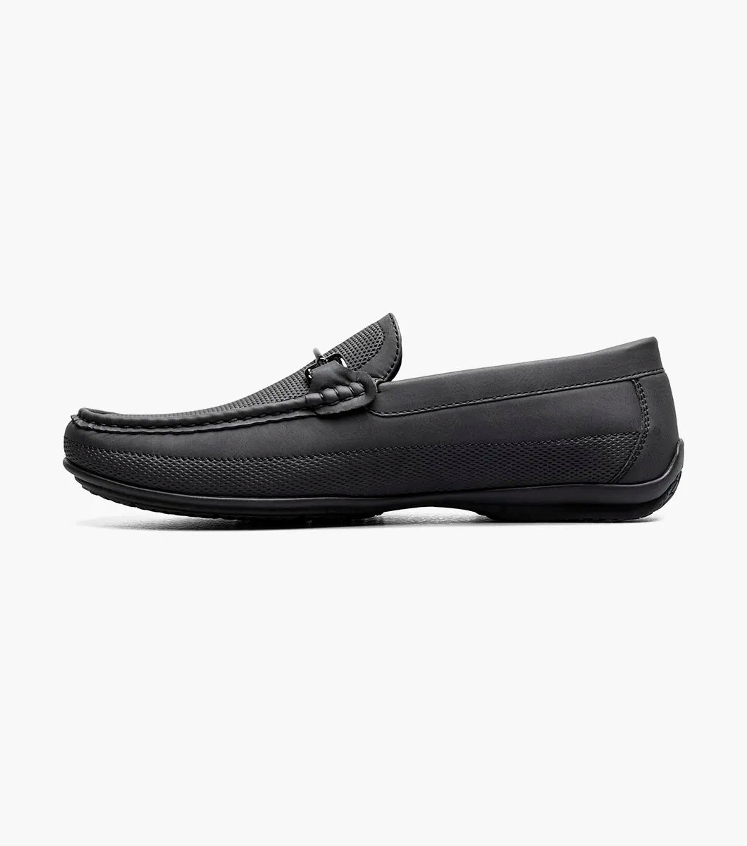The STACY ADAMS Colton Moc Toe Bit Slip On in black (25760-001) features textured leather, cushioned footbed, metal bit accent, and striped inner lining, shown on a white background.