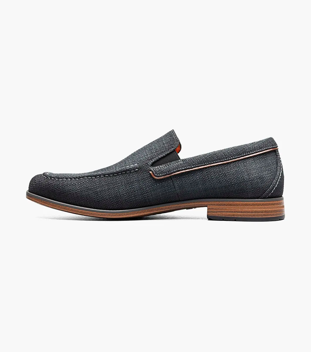 The Stacy Adams Ridgely Moc Toe Slip On in charcoal features visible stitching, a low wooden heel, comfy footbed, and tan lining. Shown against a white background, this casual loafer is perfect for everyday wear.