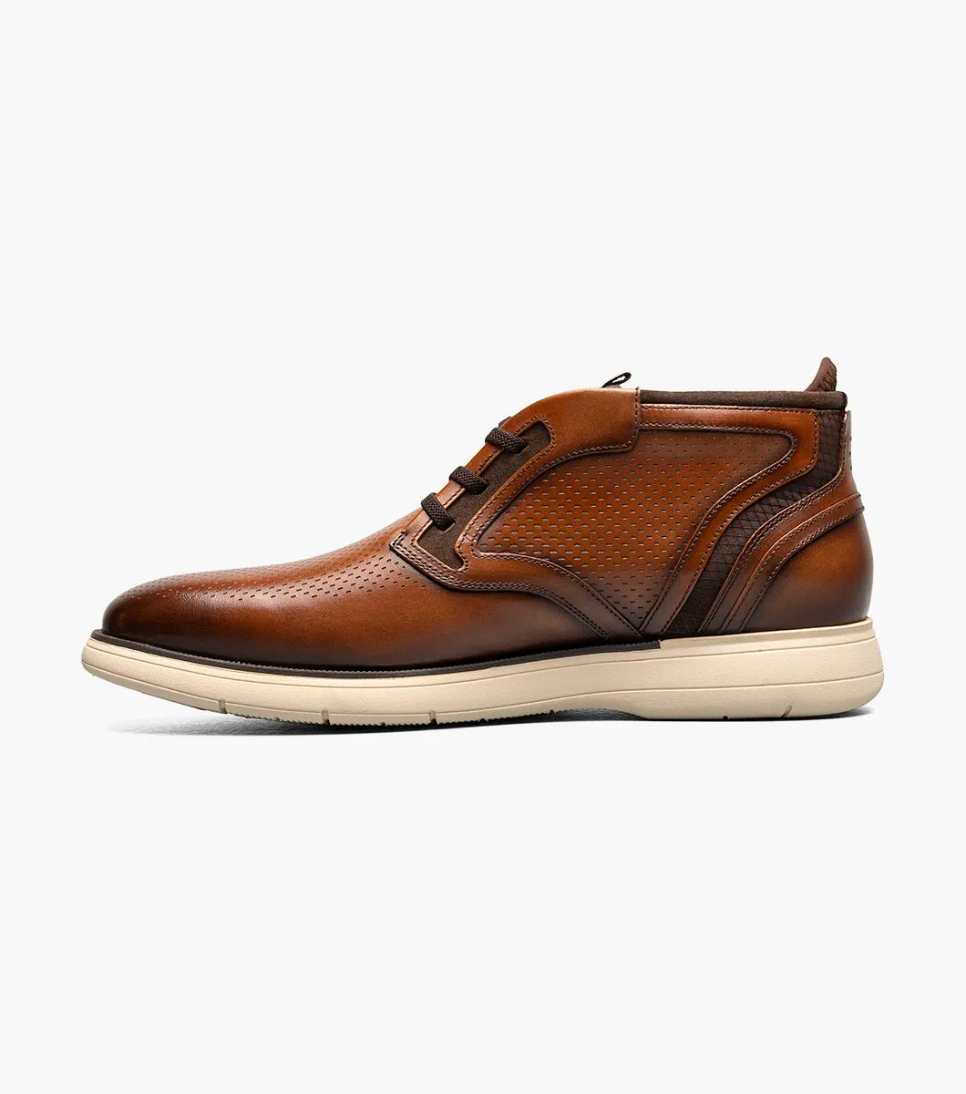 The Stacy Adams Eastmont Plain Toe Elastic Lace Chukka Boot in cognac features a perforated design, light tan rubber sole, and anatomical arch support for all-day comfort, shown on a white background.