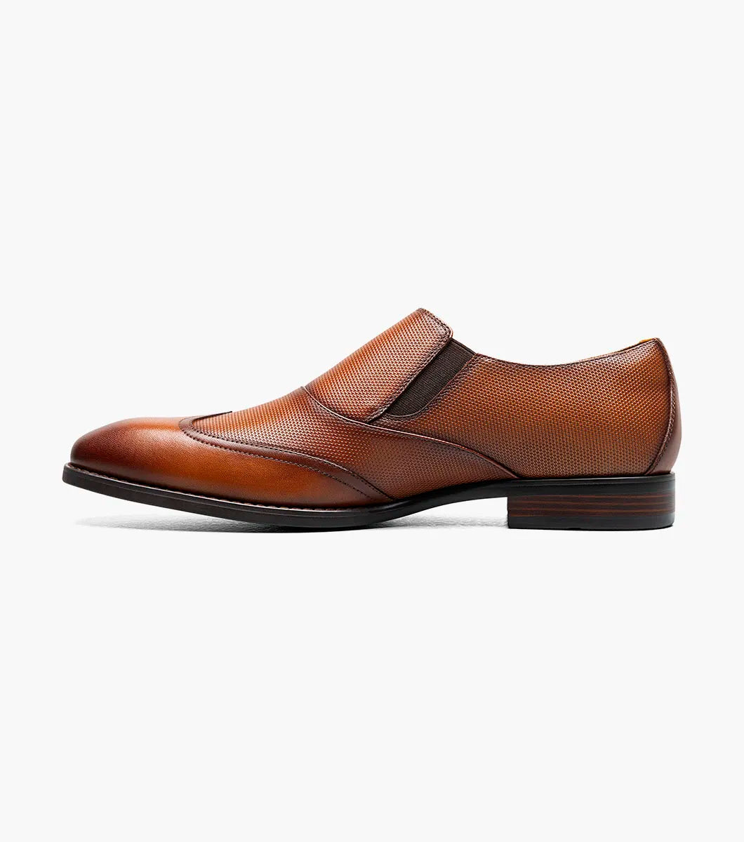 The Stacy Adams Lockwood Wingtip Ornament Slip On in Cognac features classic leather style with a textured upper, single side buckle, and low stacked heel—perfect for men seeking timeless dress shoes.