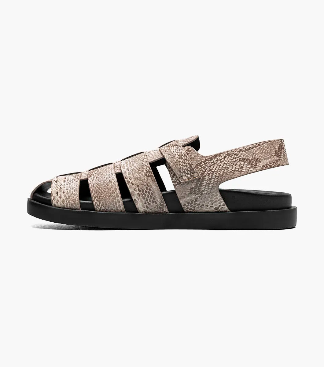 The Stacy Adams Montego Slingback Buckle Sandal (Sand, 25659-269) features a tan snakeskin pattern, closed toe, cutout sides, adjustable buckle strap, black sole, and cushioned EVA midsole on a white background.
