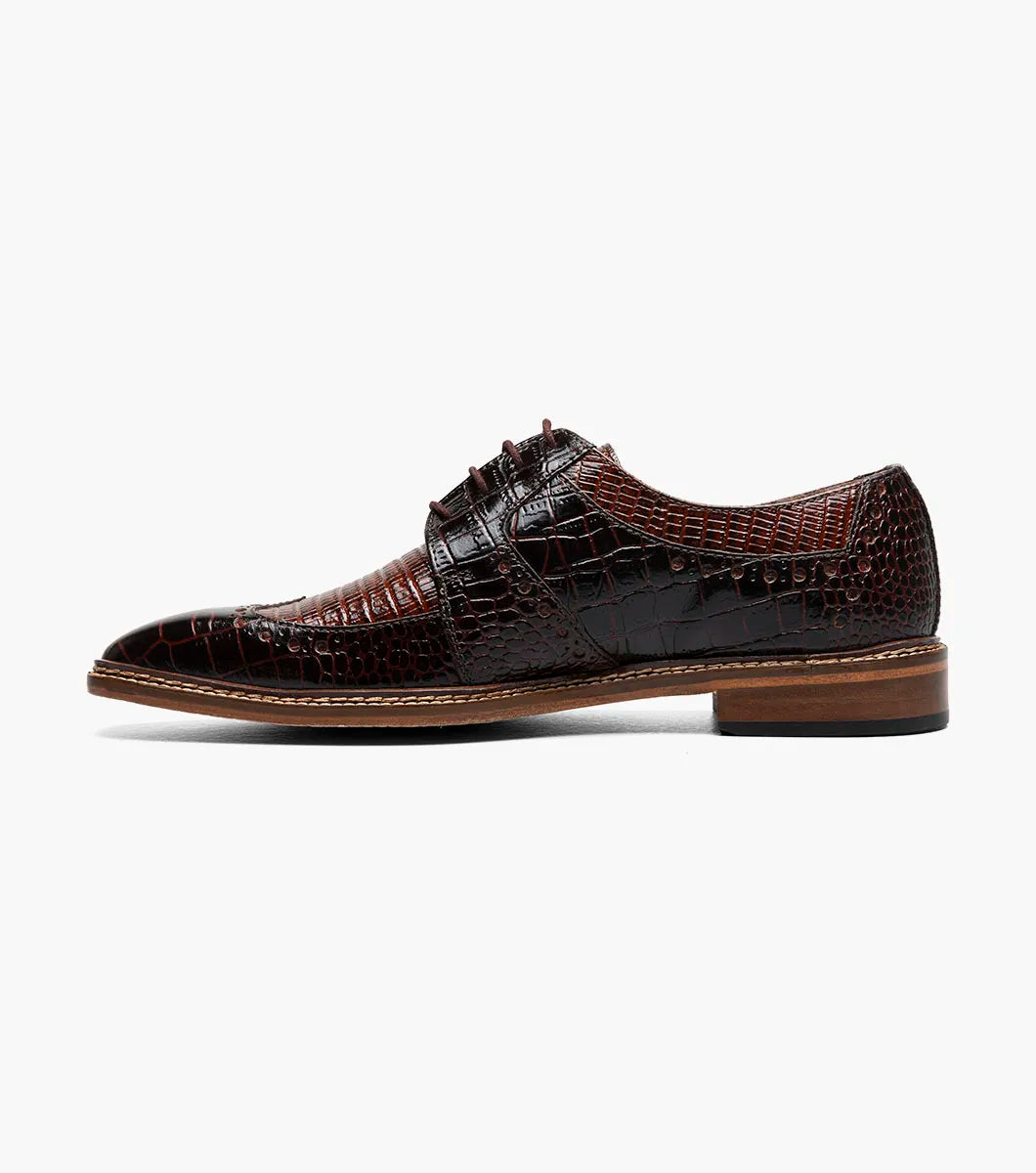 The STACY ADAMS Travato Wingtip Oxford (Brown Multi, 25737-249) features a crocodile-patterned leather upper, laces, and a wooden sole, shown at an angle on a plain white background.