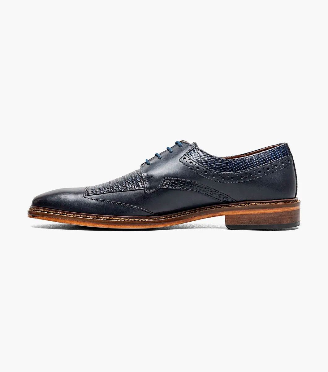 The STACY ADAMS Gambetta Modified Cap Toe Oxford (Navy, 25780-410) is a navy blue leather dress shoe featuring a textured pattern, brown sole, RedZone footbed, and lace-up closure, displayed on a white background.
