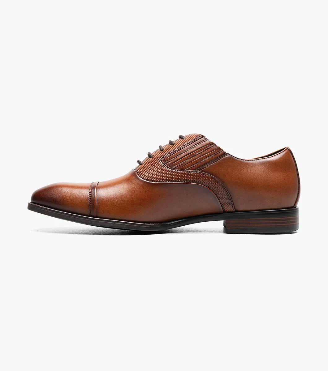 The Stacy Adams Lucas Cap Toe Oxford in Cognac (25766-221) features a brown leather upper with textured side panels, lace-up closure, and low stacked heel for stylish comfort. Men's dress shoe shown on a white background.