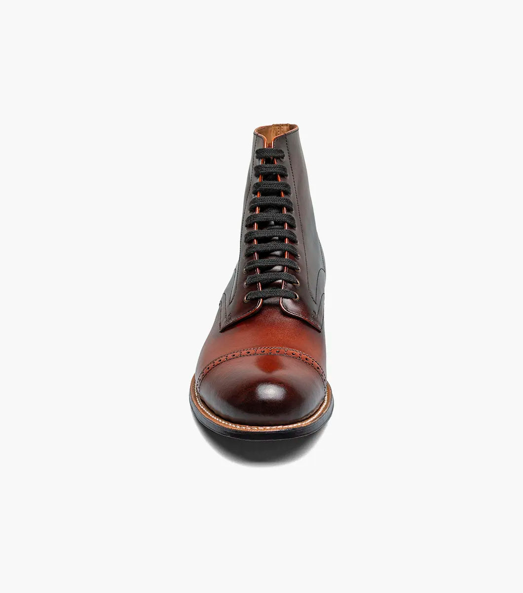 The Stacy Adams Madison Cap Toe Lace Up Boot in Cognac (00110-221) features brown leather, black laces, brogue detailing, and a stacked heel. This stylish STACY ADAMS boot is shown on a white background.
