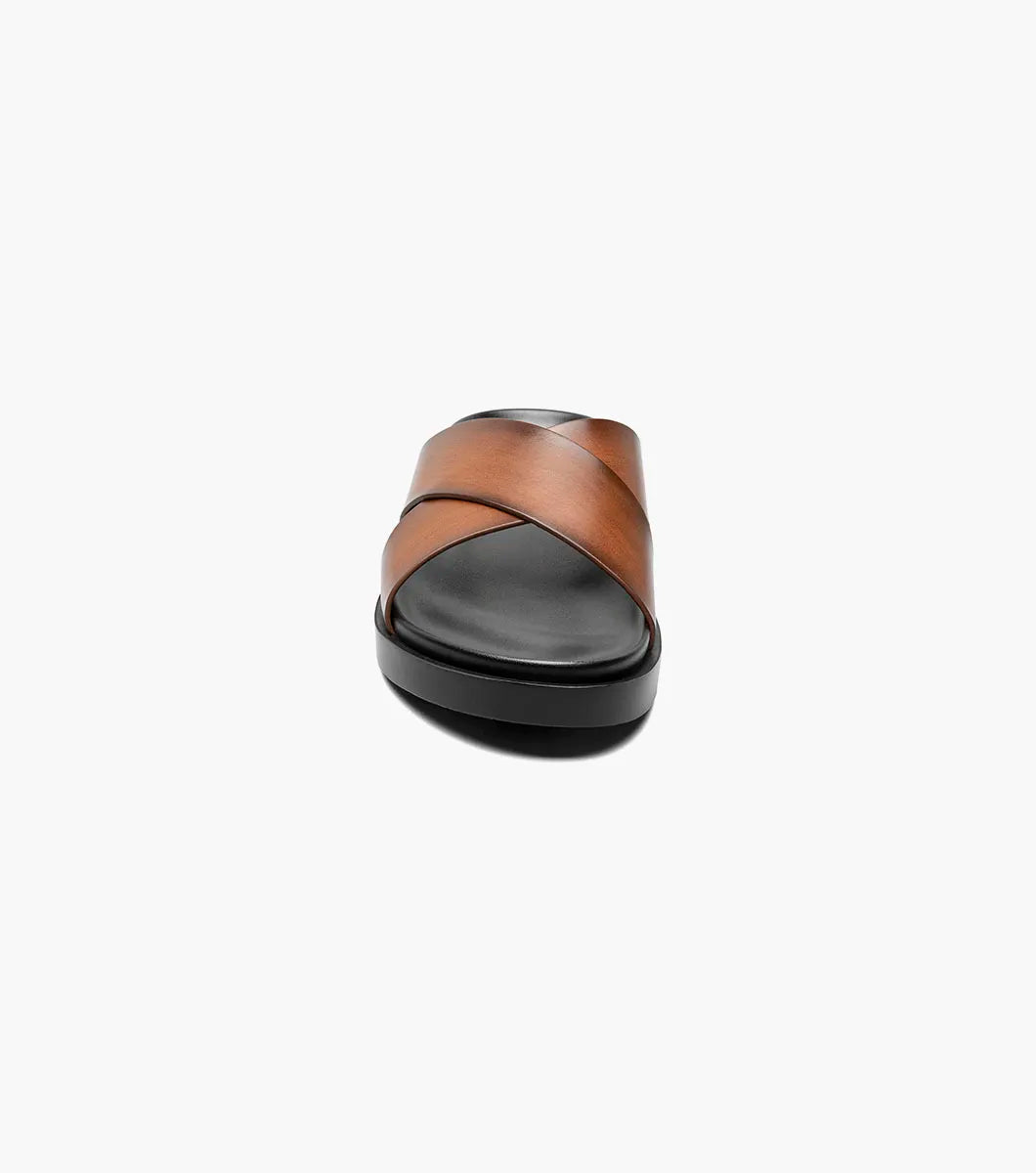 The Stacy Adams Montel Cross Strap Slide Sandal in Cognac (25469-221) features brown leather straps and a black cushioned footbed, perfect for summer. Shown on a white background.