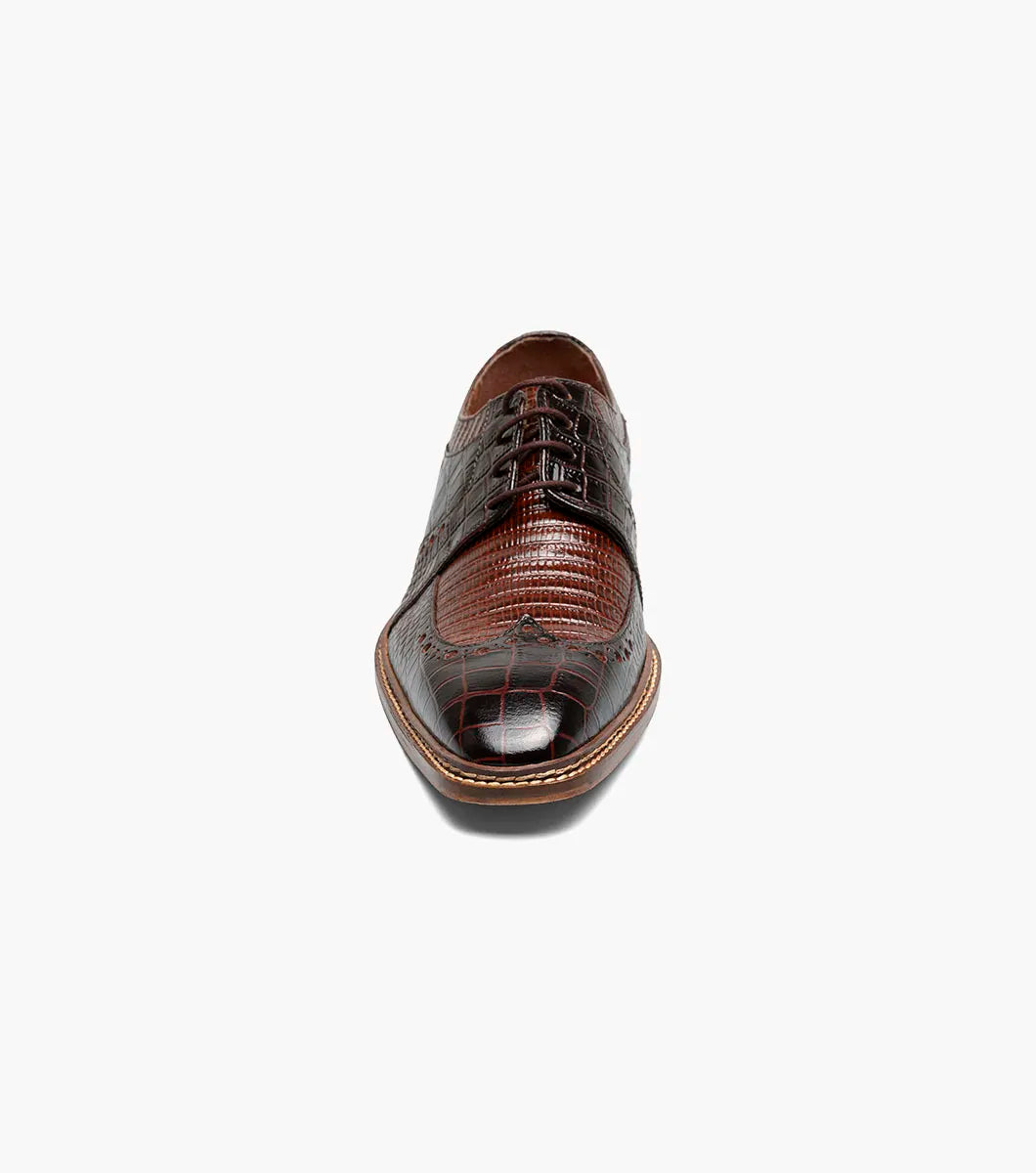 The STACY ADAMS Travato Wingtip Oxford (Brown Multi, 25737-249) features a crocodile-patterned leather upper, laces, and a wooden sole, shown at an angle on a plain white background.