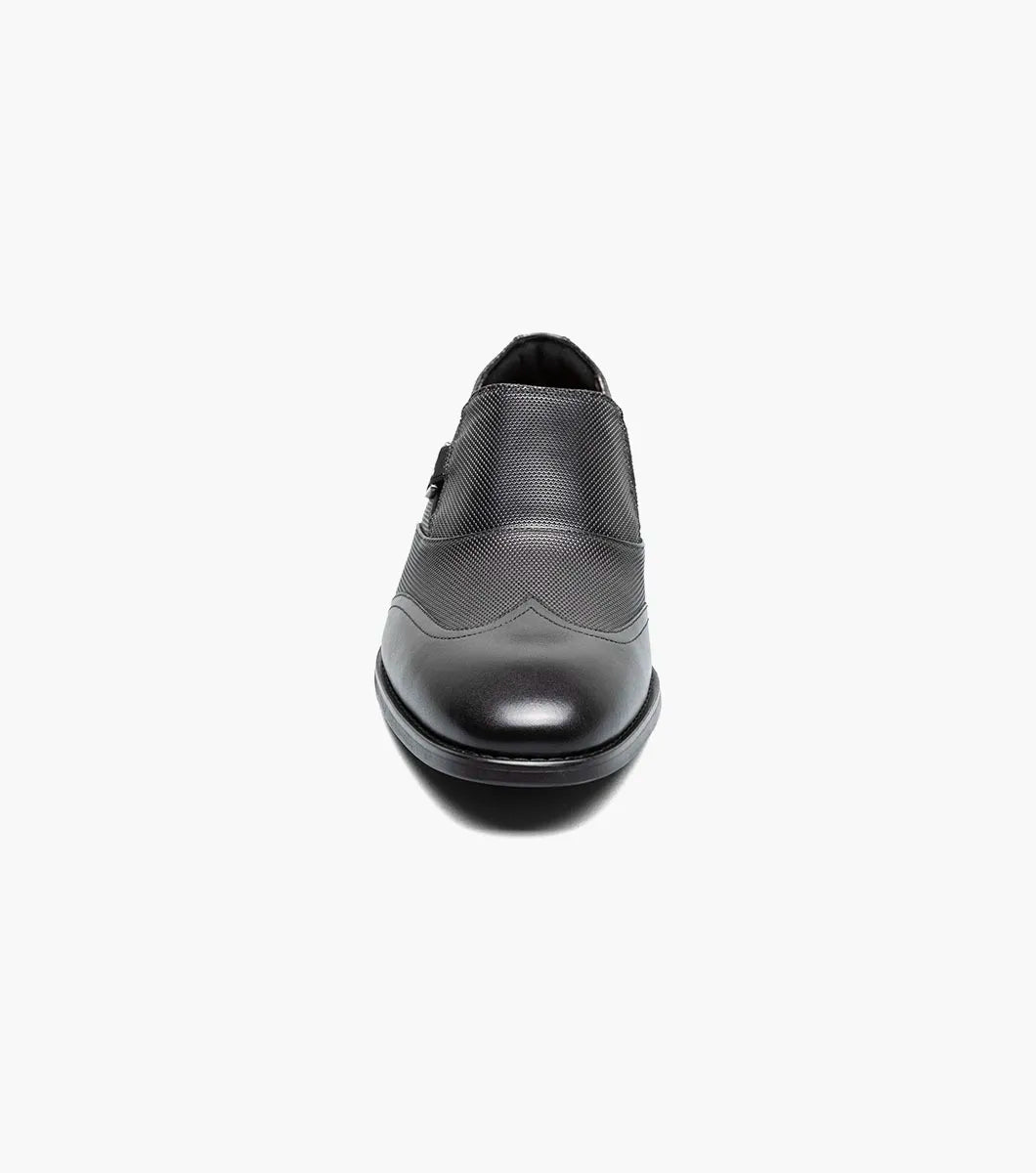 The STACY ADAMS Lockwood Wingtip Ornament Slip On in black (25767-001) features a textured upper, wingtip design, and is displayed on a white background.