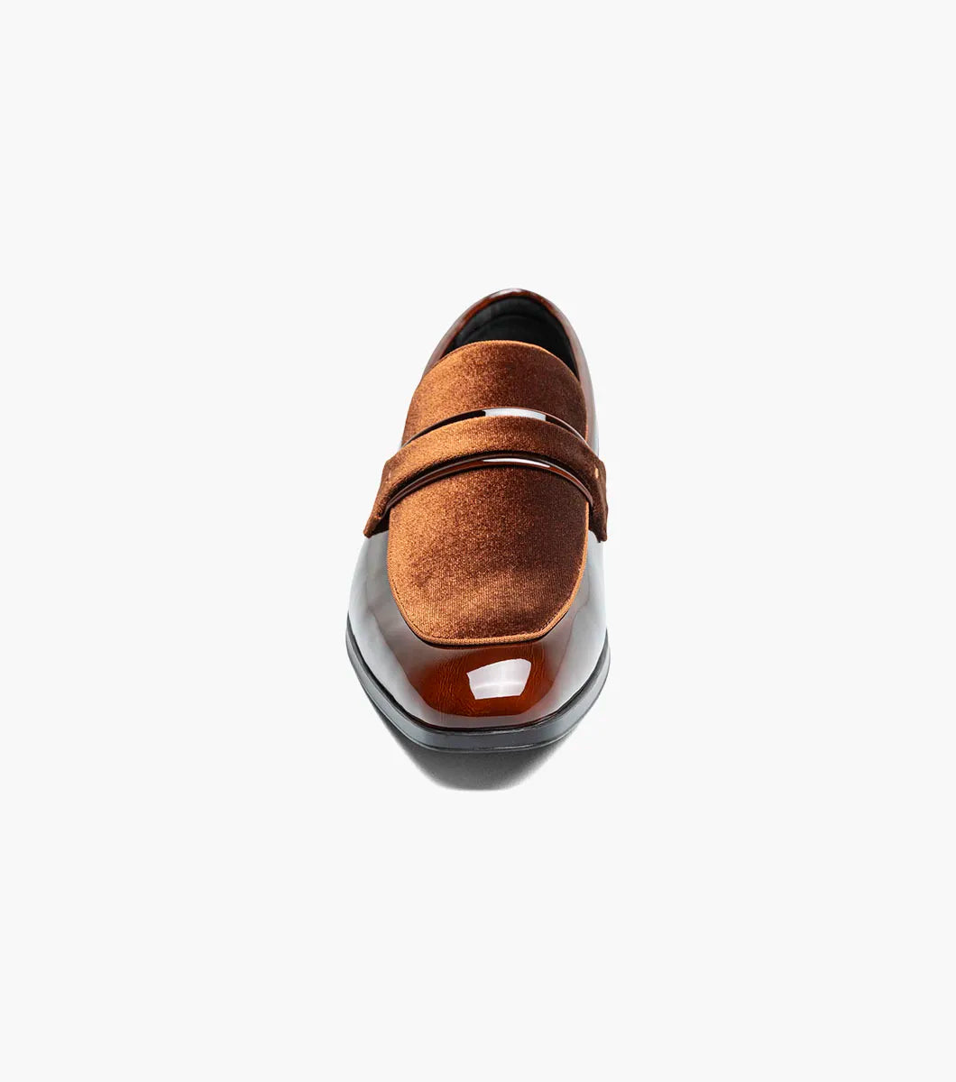 The Stacy Adams Spratley Moc Toe Saddle Slip On (Brown, 25686-200) is a men’s loafer with a glossy leather finish, cushioned insole, and velvet strap detail, displayed angled on a plain white background.