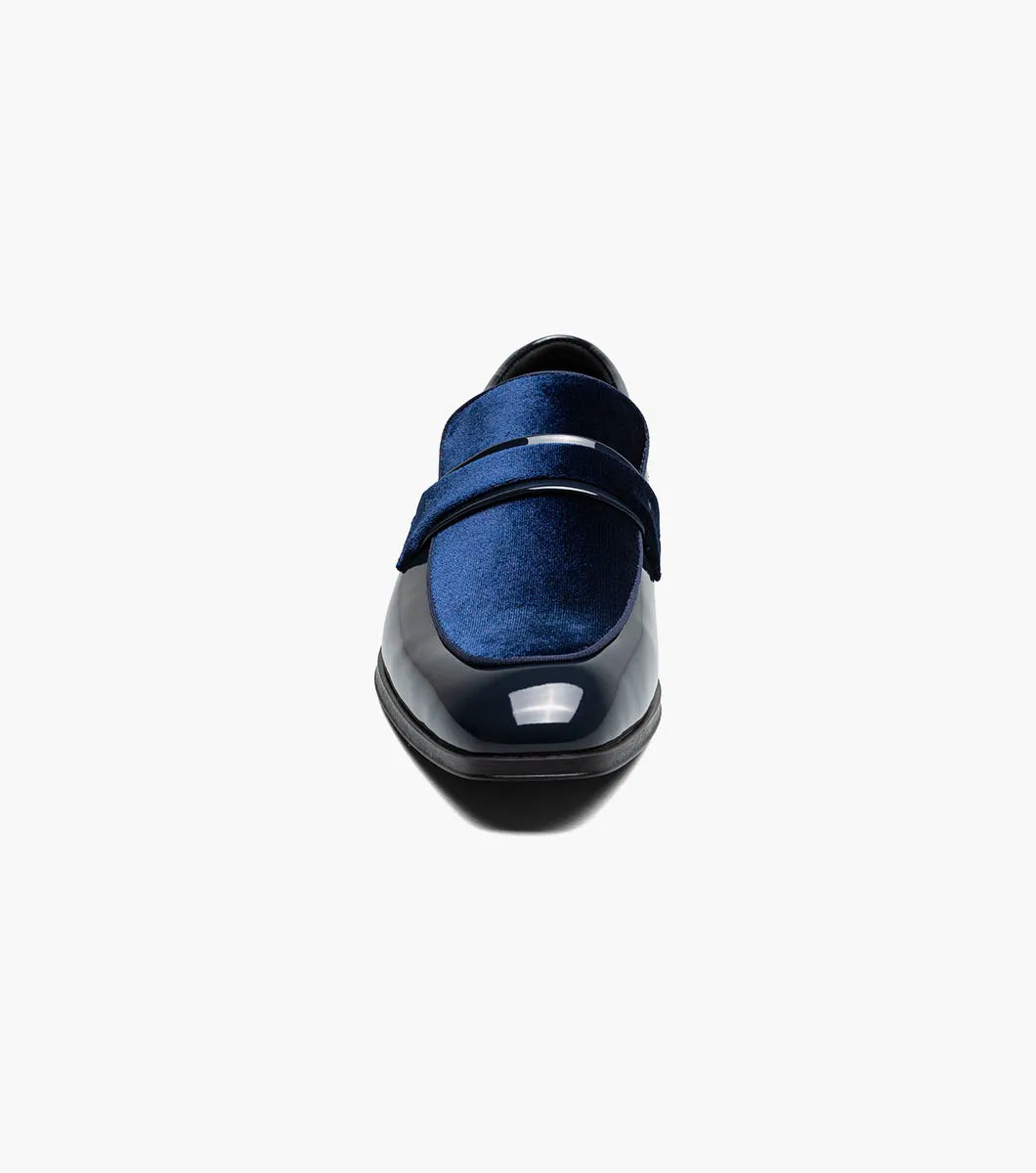The Stacy Adams Spratley Moc Toe Saddle Slip On (25686-410) features shiny navy blue leather, a matching velour upper, cushioned insole, and low black heel. Displayed solo on a white background.