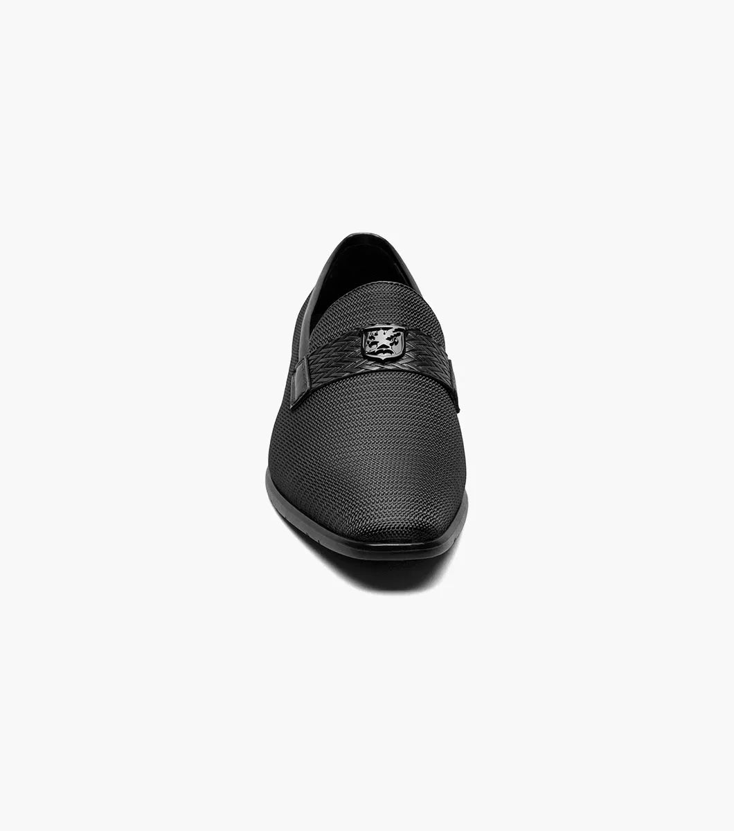 The STACY ADAMS Tazzi Plain Toe Saddle Ornament Slip On (25529-001) is a black textured men’s loafer with leather linings, Memory Foam footbed, decorative saddle band and emblem, and low heel—shown on a plain white background.