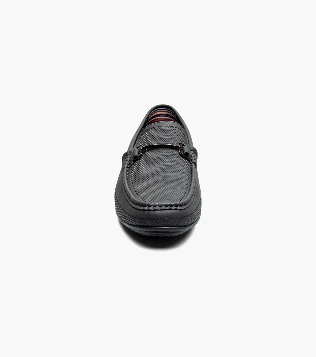 The STACY ADAMS Colton Moc Toe Bit Slip On in black (25760-001) features textured leather, cushioned footbed, metal bit accent, and striped inner lining, shown on a white background.