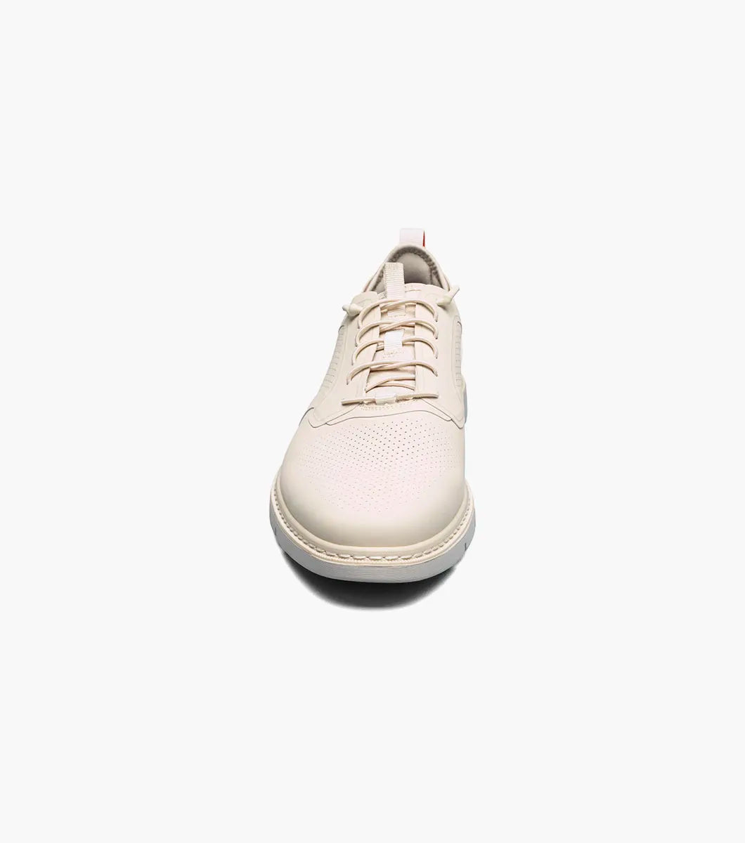 The STACY ADAMS Synchro Plain Toe Elastic Lace Up in cream (25518-113) is a leather dress shoe with perforated detailing, a gray sole, elastic laces, and a red heel pull tab, shown on a white background.