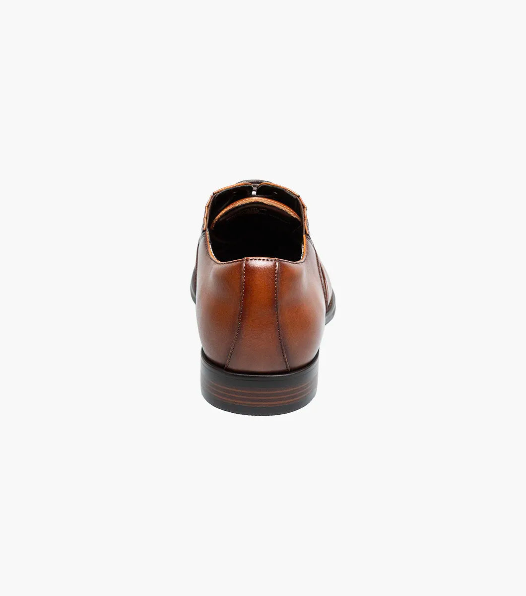 The Stacy Adams Lucas Cap Toe Oxford in Cognac (25766-221) features a brown leather upper with textured side panels, lace-up closure, and low stacked heel for stylish comfort. Men's dress shoe shown on a white background.