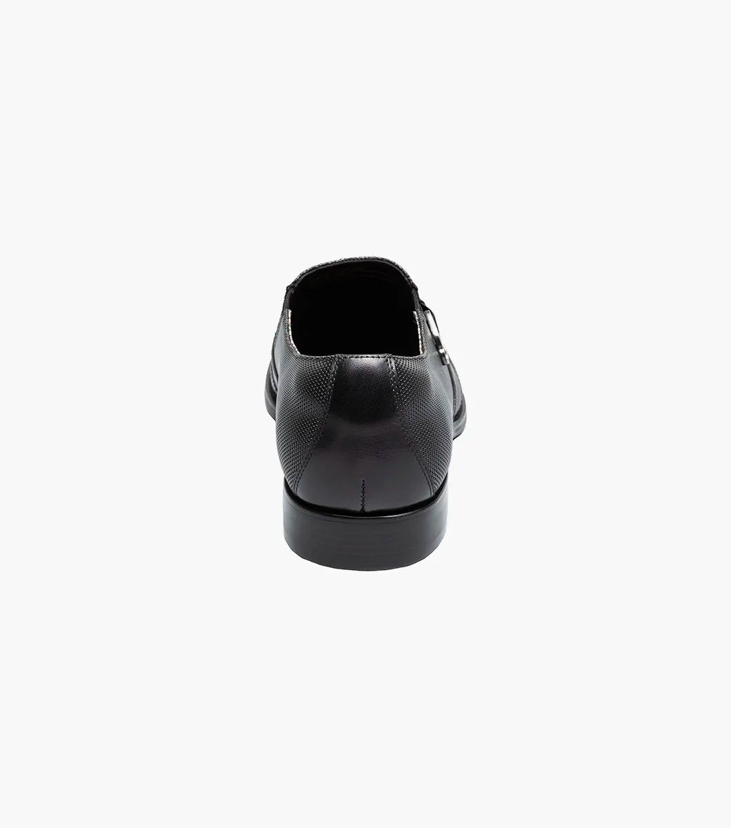 The STACY ADAMS Lockwood Wingtip Ornament Slip On in black (25767-001) features a textured upper, wingtip design, and is displayed on a white background.