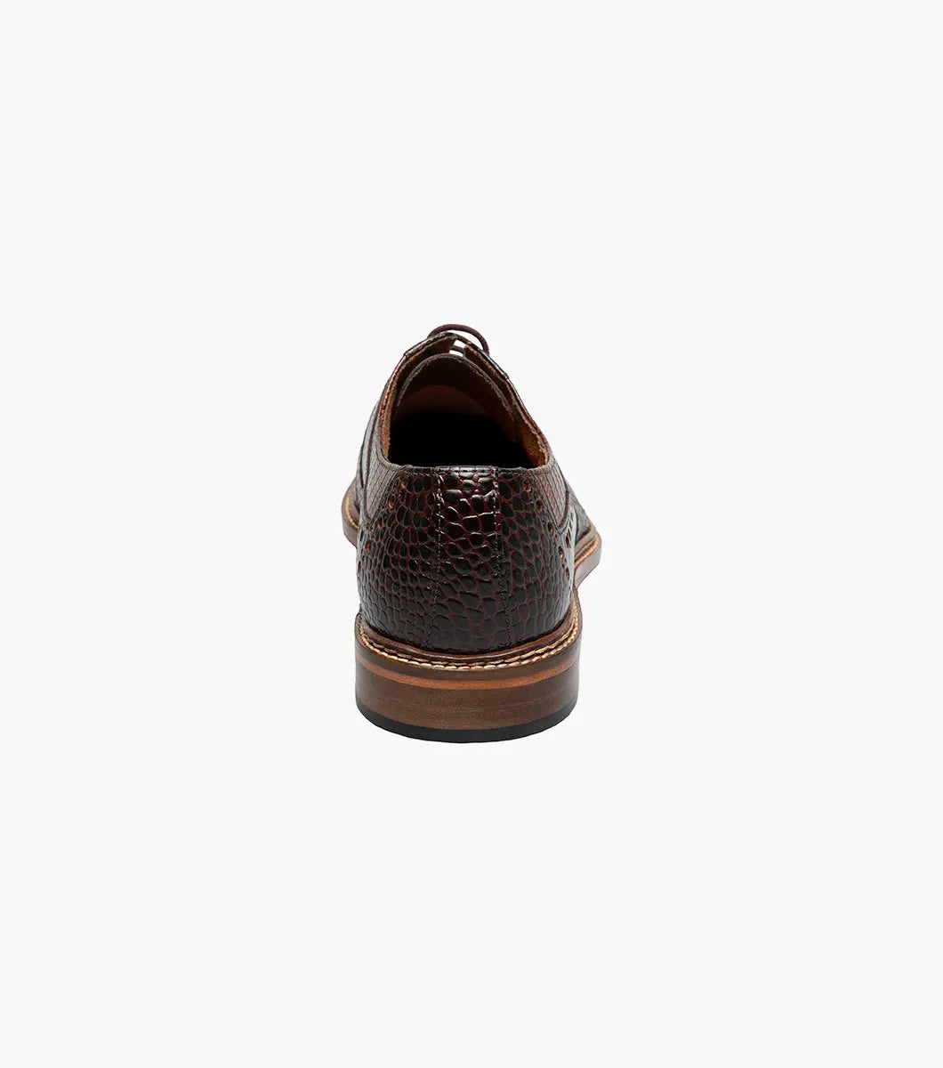 The STACY ADAMS Travato Wingtip Oxford (Brown Multi, 25737-249) features a crocodile-patterned leather upper, laces, and a wooden sole, shown at an angle on a plain white background.