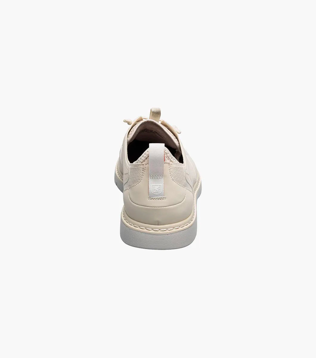 The STACY ADAMS Synchro Plain Toe Elastic Lace Up in cream (25518-113) is a leather dress shoe with perforated detailing, a gray sole, elastic laces, and a red heel pull tab, shown on a white background.