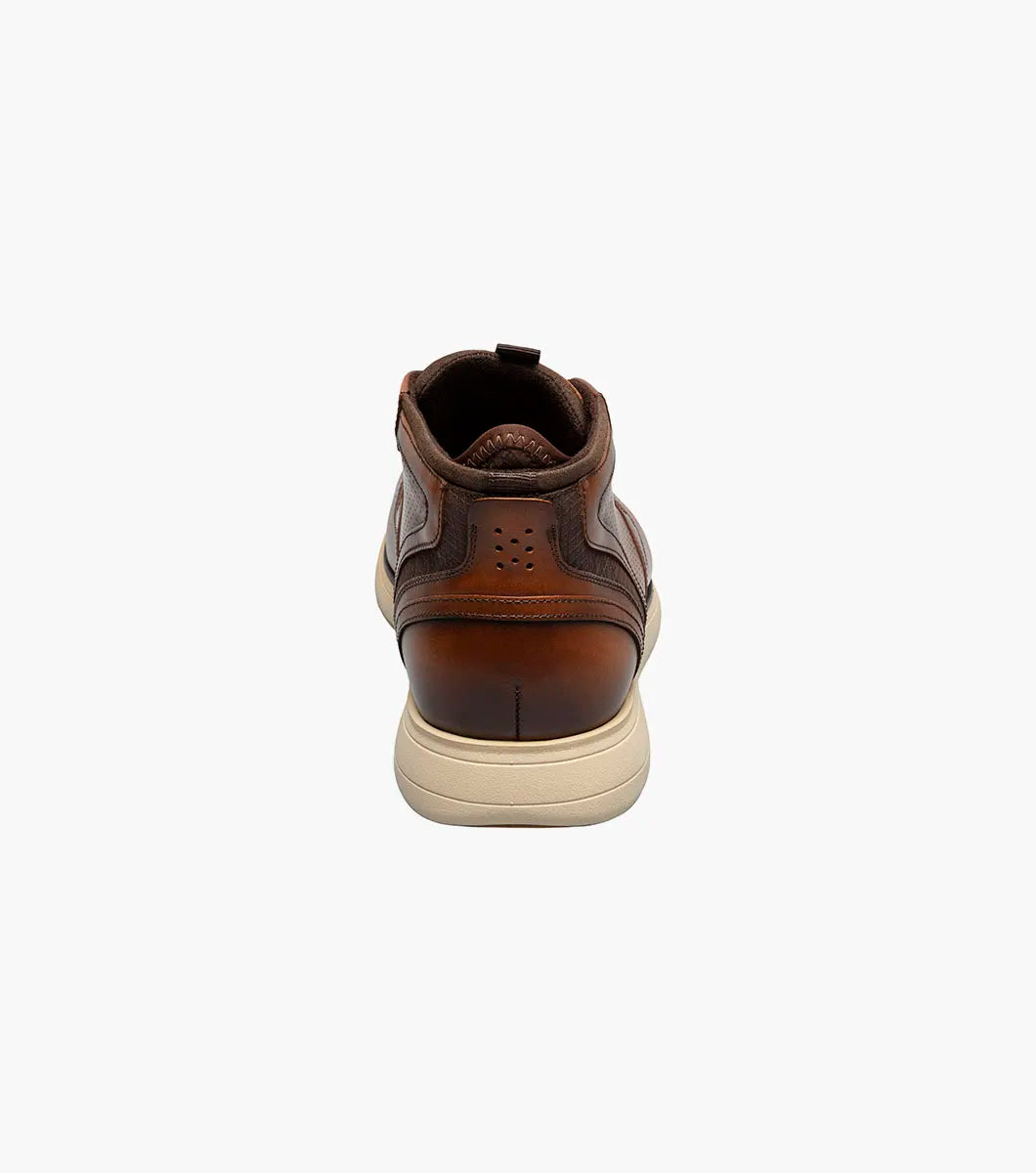 The Stacy Adams Eastmont Plain Toe Elastic Lace Chukka Boot in cognac features a perforated design, light tan rubber sole, and anatomical arch support for all-day comfort, shown on a white background.