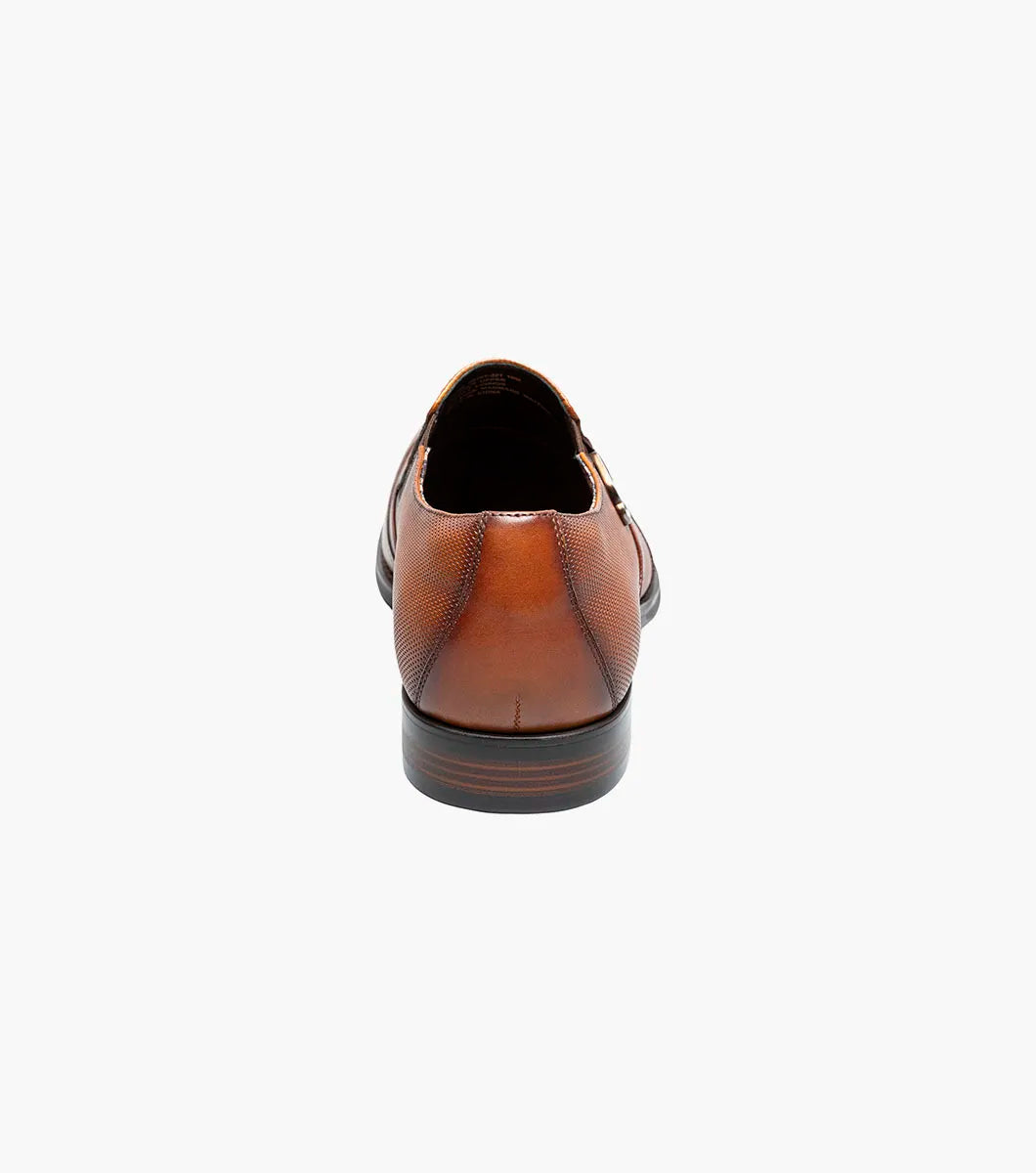 The Stacy Adams Lockwood Wingtip Ornament Slip On in Cognac features classic leather style with a textured upper, single side buckle, and low stacked heel—perfect for men seeking timeless dress shoes.