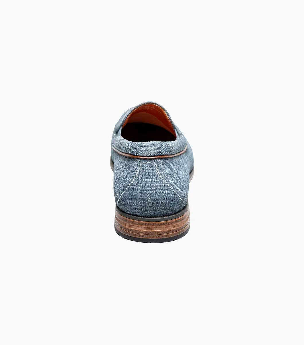 The Stacy Adams Ridgely Moc Toe Slip On in navy features a textured fabric upper, breathable leather lining, brown trim, and a low stacked wooden heel, shown against a white background.