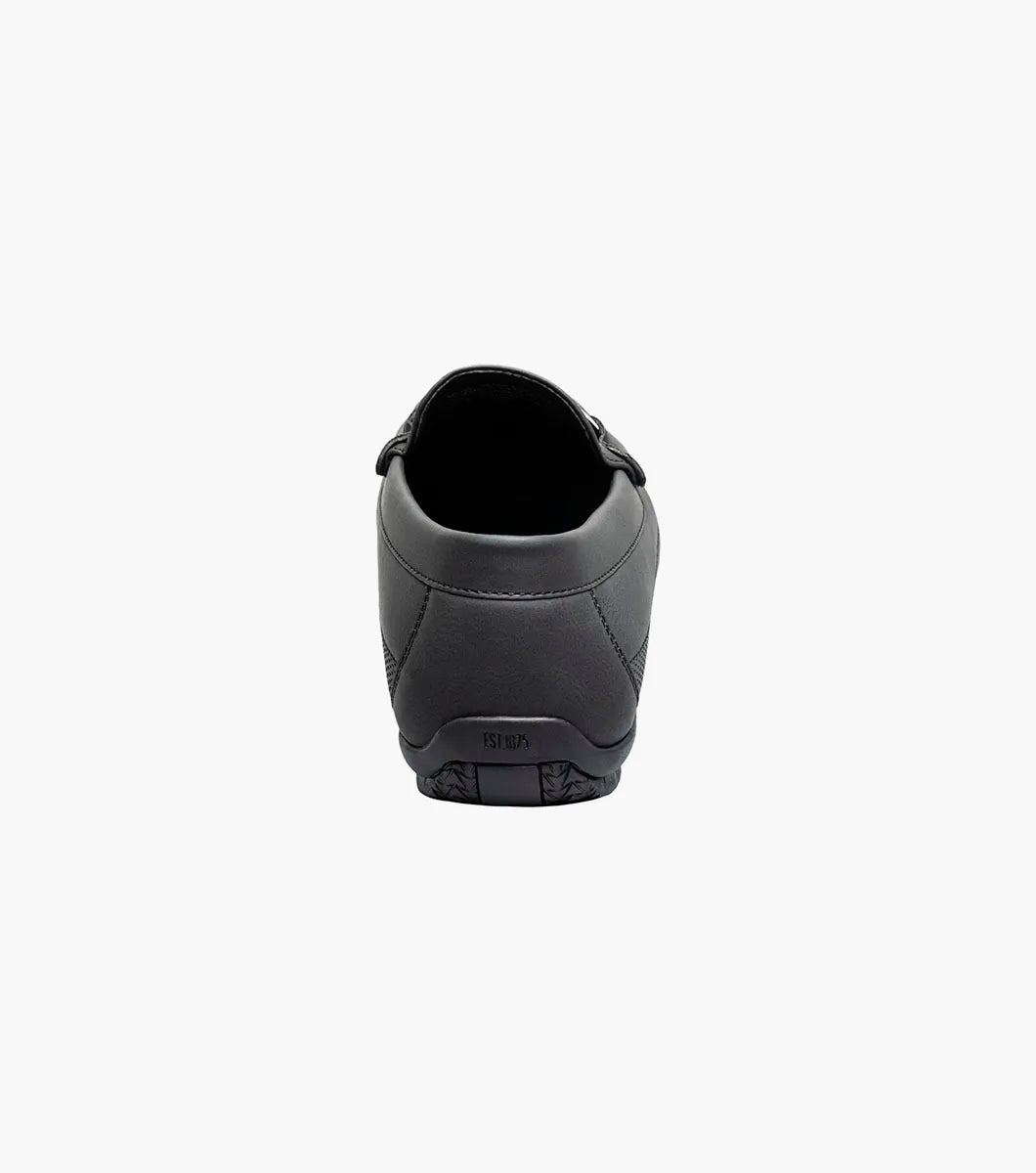 The STACY ADAMS Colton Moc Toe Bit Slip On in black (25760-001) features textured leather, cushioned footbed, metal bit accent, and striped inner lining, shown on a white background.