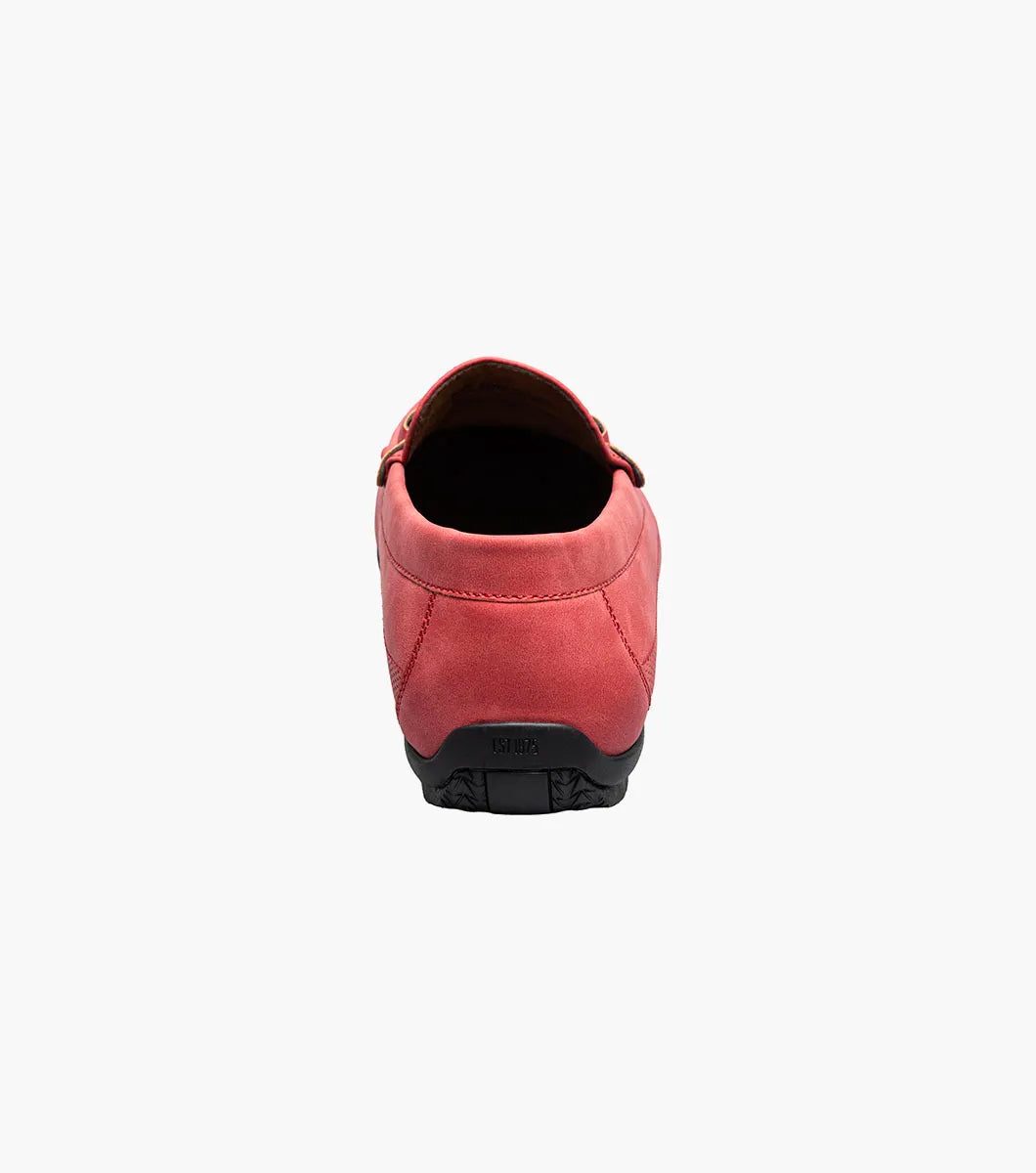 The Stacy Adams Colton Moc Toe Bit Slip On (25760-600) is a red suede loafer featuring a metal bit detail, visible stitching, black sole, striped inner lining, and cushioned footbed for comfort.
