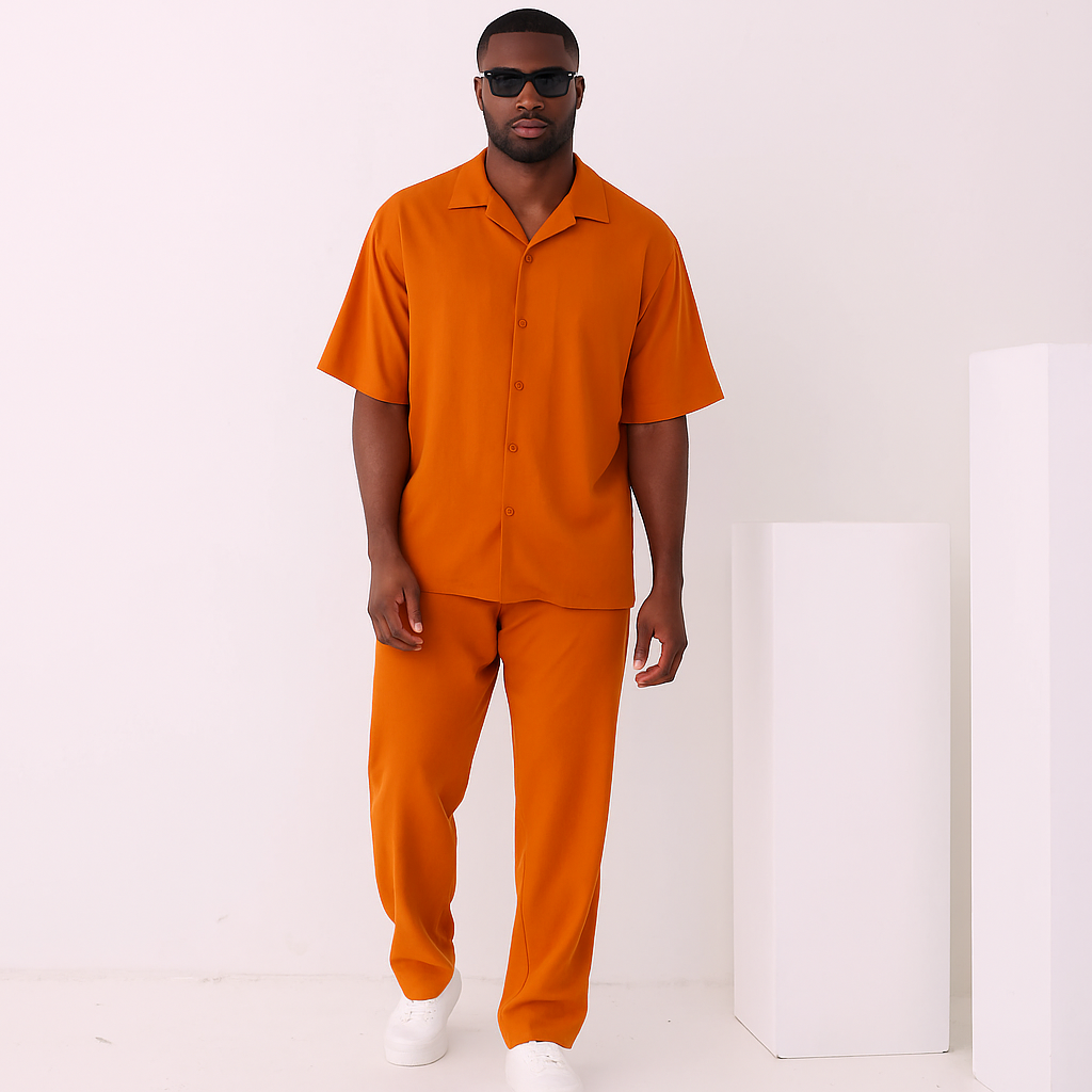 A man wearing the Inserch 2pc Set (Shirts and Pants) in Burnt Orange by Inserch stands by a doorway, holding the door frame with one hand and wearing sunglasses.
