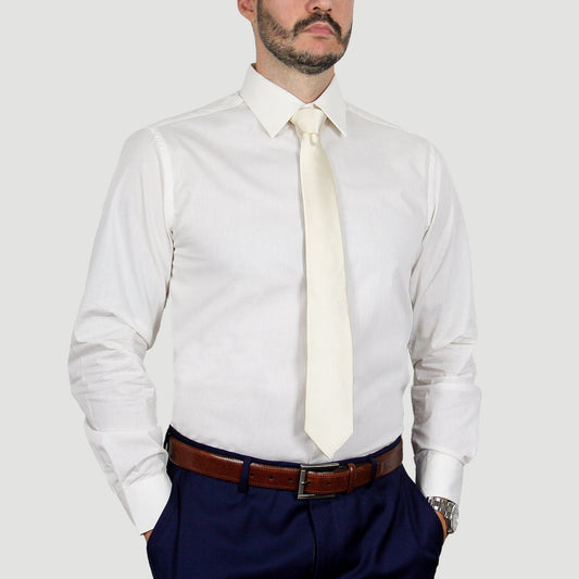 A man wearing the ARTURO Modern Fit Long Sleeve Ivory Dress Shirt, complemented by a cream tie, a brown belt, and dark polyester pants stands with hands in pockets.