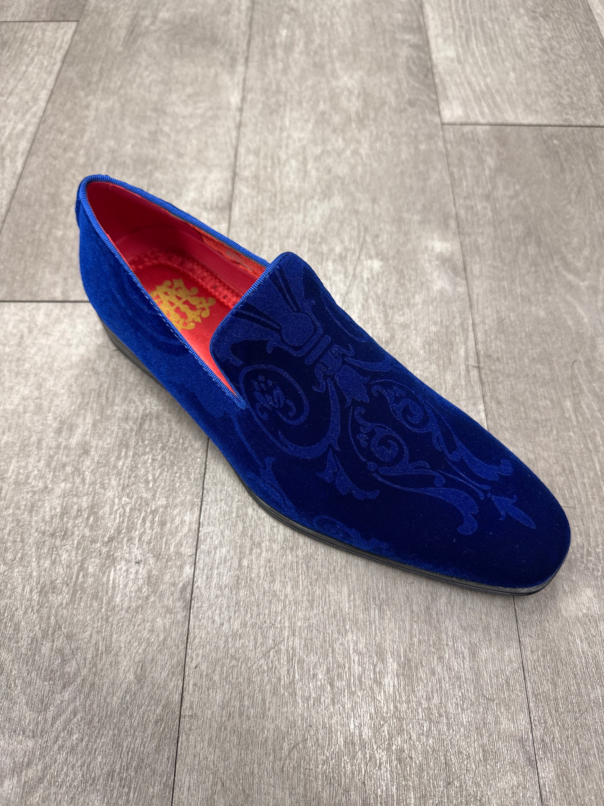 The AFTER MIDNIGHT After Midnight 7017 Royal Paisley in blue velvet, with intricate floral patterns and a loafer accent, rests elegantly on a gray wooden floor.