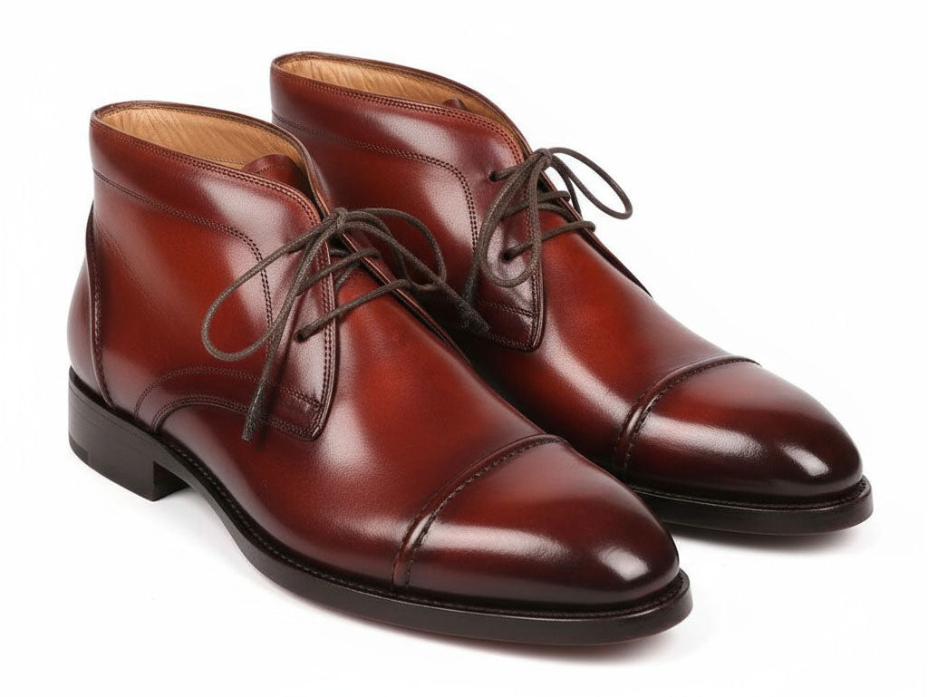 The Paul Parkman Cap Toe Chukka Boots Brown - 144BRW68, polished brown leather dress boots with laces, feature Goodyear welt construction and are displayed on a white background—one upright, the other leaning against it.