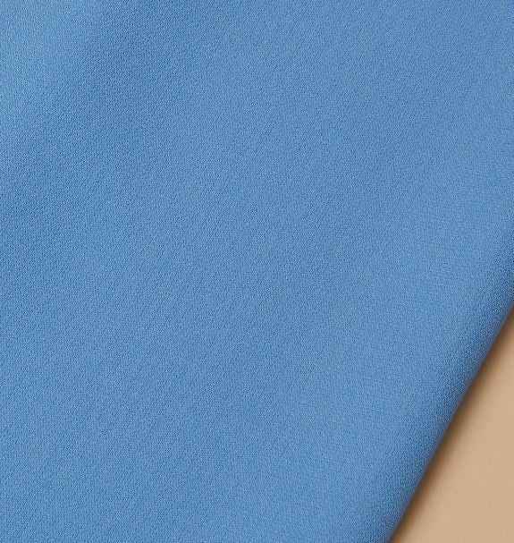 A close-up of the Inserch 2pc Set (Shirts and Pants) in Blue Mist by Inserch, highlighting the smooth high twist polyester fabric draped over a beige surface with its texture and precise edge on display.